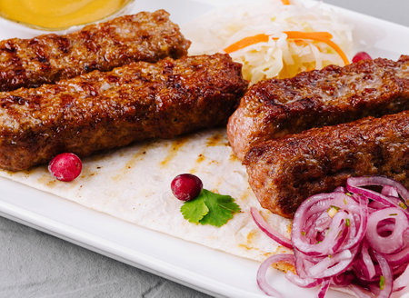 Juicy grilled kebabs served on a white plate with fresh salad and dipping sauceの写真素材