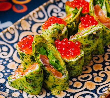 Elegant spinach crepes, filled with salmon and topped with red caviar, presented on a decorative plateの写真素材