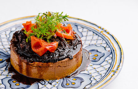 Exquisite upside-down tarte tatin decorated with strawberries and herbs on a patterned plateの写真素材