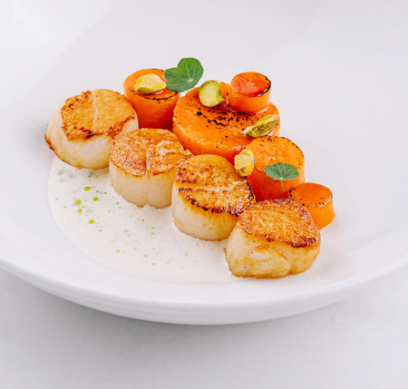 Gourmet seared scallops with herbs and garnish served on a sleek white dishの写真素材