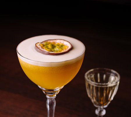 A sophisticated passion fruit cocktail in a coupe glass beside a small shot glass, showcased on a dark, wooden bar topの写真素材