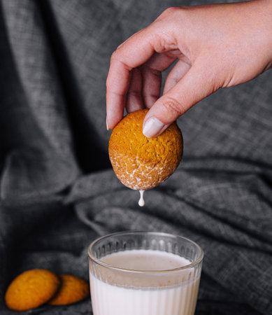 Hand dipping a freshly-baked cookie into a glass of milk, with crumbs and cookies in the backgroundの写真素材