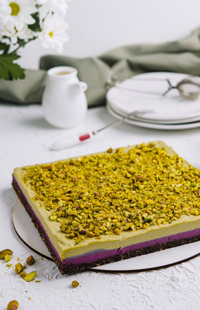 Delicious pistachio cake paired with tea on a white table, complemented by fresh flowersの写真素材