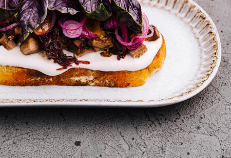 Artisanal toast topped with cream cheese, caramelized onions, and fresh purple basil on ceramic plateの写真素材