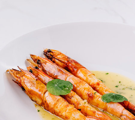 Succulent grilled shrimp with a garlic butter sauce garnished with fresh basil, served on a modern white plateの写真素材