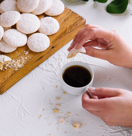 Close-up of hands holding coffee beside powdered sugar cookies on a wooden boardの写真素材