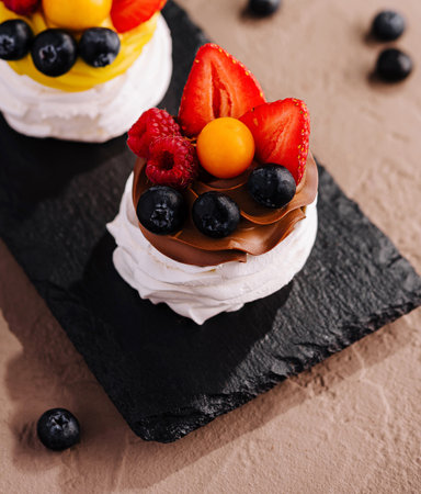Three mini pavlovas with whipped cream and fresh berries on a stylish slate serving boardの写真素材