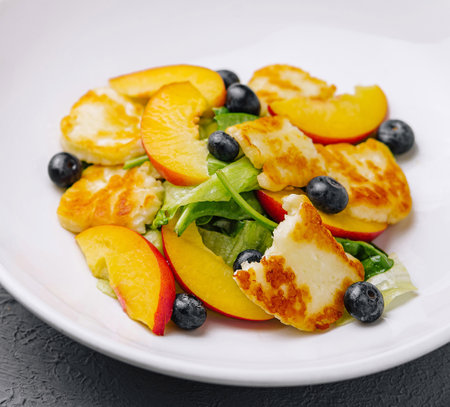Colorful fruit salad with grilled halloumi, blueberries on a dark tableの写真素材