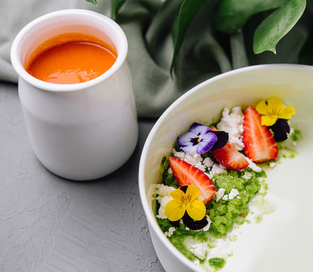 Elegant breakfast bowl with pistachio green granola, vibrant edible flowers, and fresh strawberry slicesの写真素材