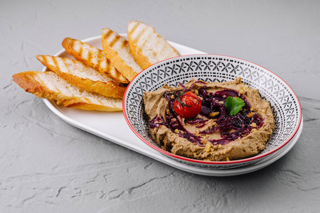 Plate of creamy hummus topped with herbs and a roasted tomato alongside golden toasted breadの写真素材