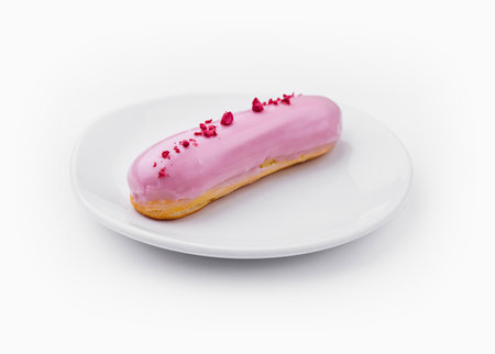 Delicious pink frosted eclair with sprinkles on a sleek white plate, isolated on white background