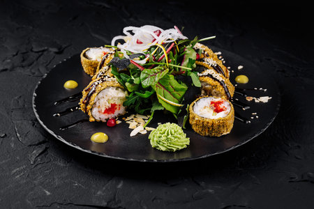 Elegant presentation of sushi rolls with fresh greens, sesame, and sauce on a black plateの写真素材