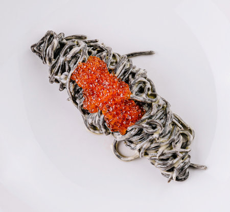 Elegant presentation of squid ink pasta topped with luxurious red caviar on a white plateの写真素材
