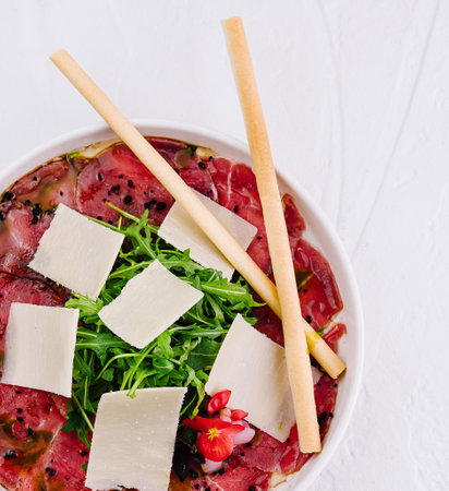 Gourmet beef carpaccio plated with arugula, parmesan slices, and breadsticksの写真素材