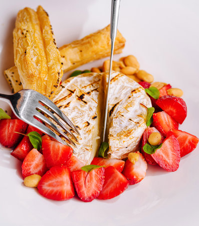 Close-up of a dish with brie cheese, strawberries, and puff pastry, being cut with a fork and knifeの写真素材