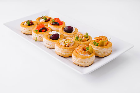 Selection of elegant mini tartlets with savory toppings on a sleek white platterの写真素材