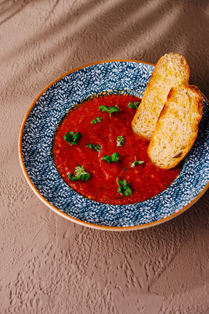 Bowl of rich tomato soup garnished with herbs, served with golden brown toasted breadの写真素材