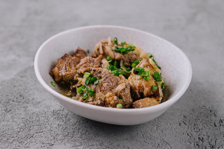 Tender chunks of braised beef garnished with green scallions in a white bowl, ready to serve
