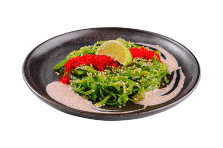 Vibrant seaweed salad with tobiko, sesame seeds, and a wedge of lime, served in a ceramic dishの写真素材