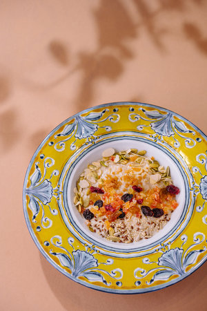 Top view of a nutritious muesli mix with dried fruits and nuts in a vibrant ceramic bowl on a pastel...
