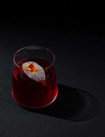 Sophisticated red cocktail with a delicate flower garnish, presented on a moody, dark surface with soft lightingの写真素材