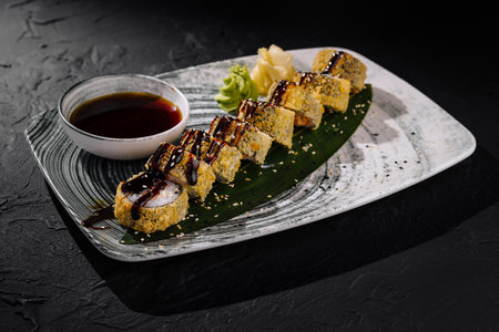 Gourmet sushi rolls adorned with sesame, served with soy sauce, ginger, and wasabi on a dark slateの写真素材