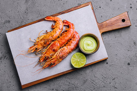 Succulent grilled prawns served with a side of lime and dipping sauce on a stylish wooden boardの写真素材
