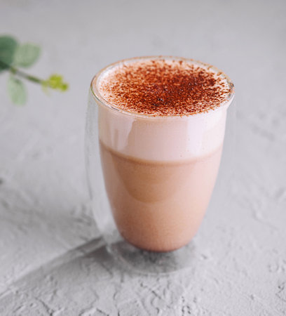 Aromatic milk tea latte topped with spices, served in a clear glass, with a green plant backgroundの写真素材