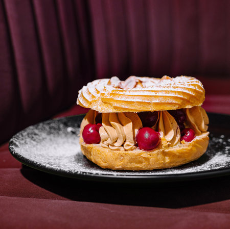 Delicious paris-brest with cream and berries on a black plate against a red backgroundの写真素材