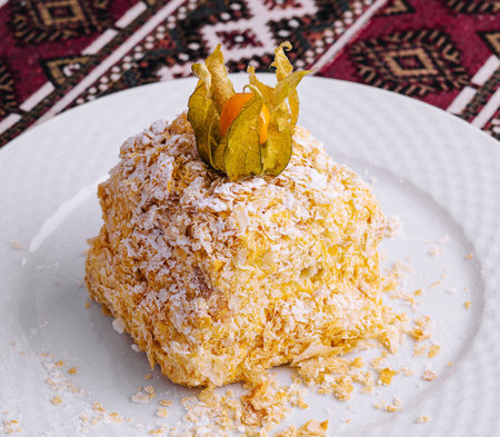 Delectable sweet napoleon cake topped with dried fruit, served on a white plate with an intricate patterned backgroundの写真素材