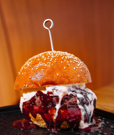 Delectable cheeseburger with a savory sauce served on a stylish black dish against a warm backgroundの写真素材