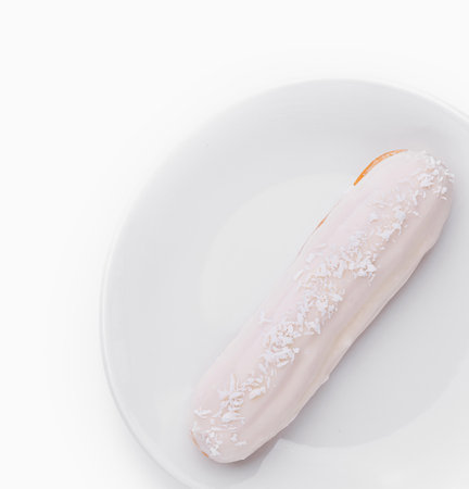 Eclair with white frosting and coconut sprinkles on a plain white plate, isolated on white backgroundの写真素材