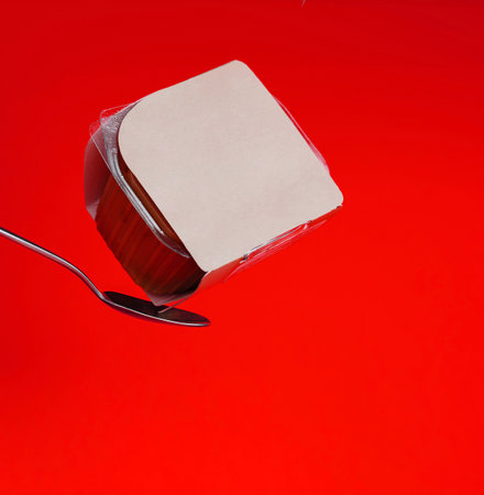 A single yogurt cup with foil lid, precariously perched on a metal spoonの写真素材
