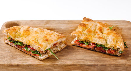 Delicious panini sandwich with tomatoes, cheese, and greens, cut and served on a wooden cutting boardの写真素材