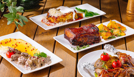 Elegant spread of diverse gourmet meals artfully plated on a rustic wooden dining surfaceの写真素材