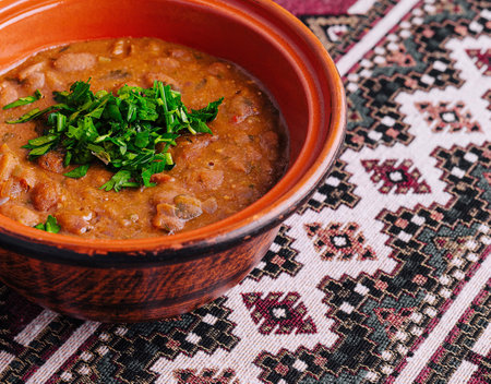 Hearty lentil soup in a rustic clay bowl, garnished with fresh parsley, on an ethnic-patterned tableclothの写真素材