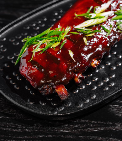 Delicious sticky bbq pork ribs garnished with fresh green onions, served on a black plateの写真素材