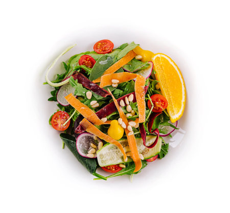 Vibrant bowl of mixed greens with tomato, cucumber, and orange slices on a clean white surfaceの写真素材