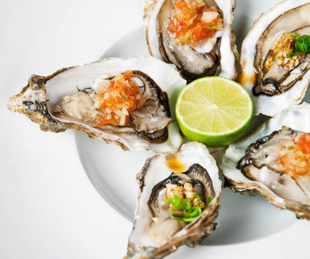 Appetizing plate of raw oysters garnished with lime and salsa on a white backgroundの写真素材