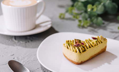 Delicious pistachio dessert on a plate with a cup of coffee in a cozy settingの写真素材