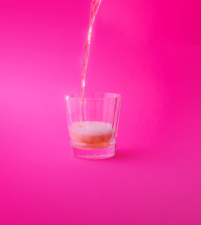 Pink drink being poured into a glass with a pink backgroundの写真素材