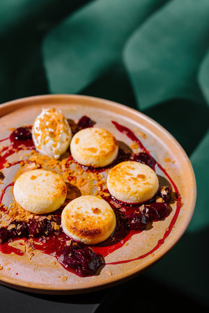 Round cottage cheese pancakes lying on a plate with cherry jam, decorated with sour cream and crumbsの写真素材