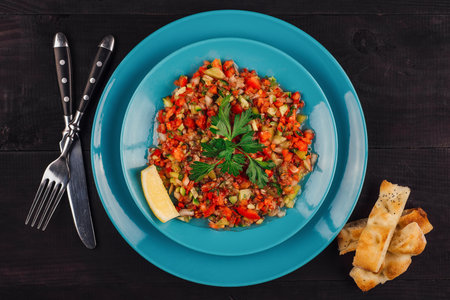 Turkish coban salad with lemon, parsley, cucumber, tomato and pita bread on turquoise plate on black wooden tableの写真素材
