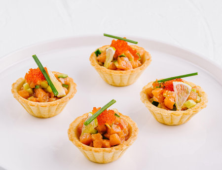 Elegant appetizer tartlets filled with salmon, caviar, and herbs presented on a white plateの写真素材