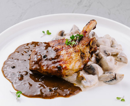 Succulent grilled pork chop with rich mushroom sauce, garnished with herbsの写真素材