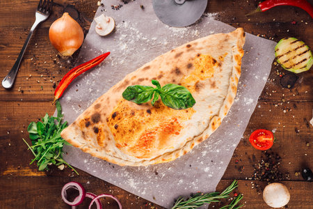 Delicious calzone lying on wooden table surrounded by fresh ingredientsの写真素材