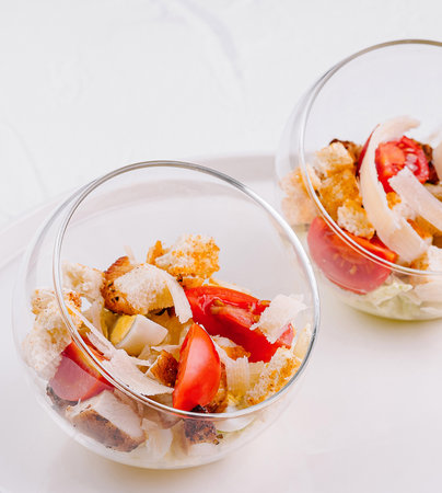 Two glass bowls with caesar salad served on a white plate and textured backgroundの写真素材