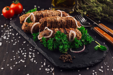 Delicious kebabs with red onions and herbs on a black slate platter, seasoned with salt and pepperの写真素材