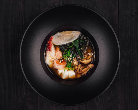 Aromatic miso soup with tofu, wakame seaweed, shiitake mushrooms and seafood served in black bowlの写真素材