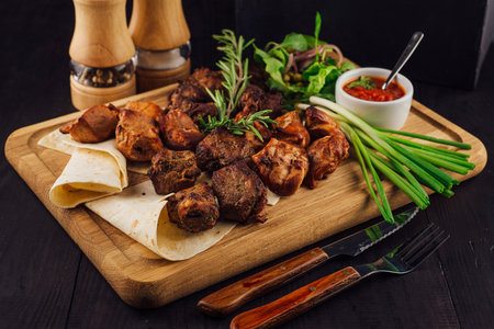 Delicious barbecued meat with onions and herbs served on a wooden board with pita bread and sauceの写真素材